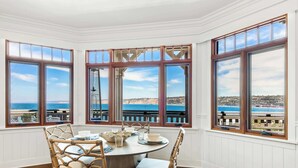 Un espace repas offrant une vue sur l’océan, de grandes fenêtres et une table ronde entourée de chaises.