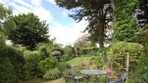 A garden with a table and chairs, surrounded by various plants and trees. - 1 Bed in Bridport (oc-dc016) (Burton Bradstock)