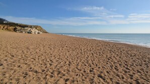A sandy beach with a clear sky and a rocky cliff in the background. - 1 Bed in Bridport (oc-dc016) (Burton Bradstock)
