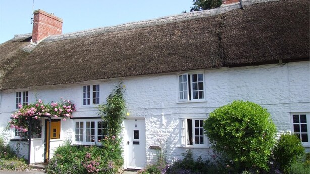 A white building with a thatched roof, multiple windows, and a door. - 1 Bed in Bridport (oc-dc016) (Burton Bradstock)