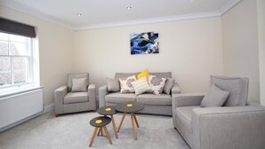 Un salon moderne avec un canapé gris, deux fauteuils, une table basse et un tableau accroché au mur.