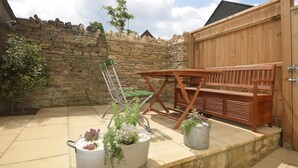Une terrasse avec une table et des chaises en bois, un mur en pierre et des plantes en pot.