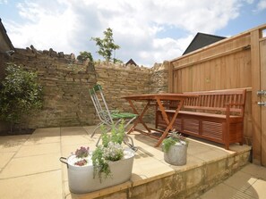 Eine Terrasse mit Holztisch und -stühlen, einer Steinmauer und Kübelpflanzen.