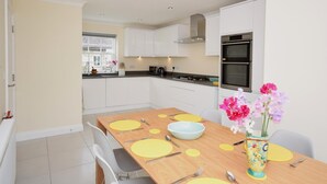 Une cuisine moderne avec des meubles blancs, une table à manger en bois agrémentée de sets de table jaunes et un vase rempli de fleurs.