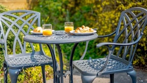 Dos sillas metálicas y una mesa con alimentos para el desayuno, incluyendo cruasanes y jugo de naranja.