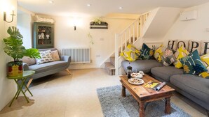 A cozy living room with a grey sofa, a wooden coffee table, and a staircase leading to another level. - 3 Bed in Bridport (oc-dc080) (Charmouth)