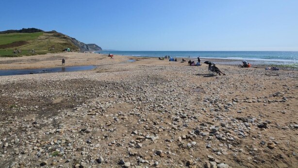 A pebbly beach with people and tents, a clear sky, and a distant hill. - 3 Bed in Bridport (oc-dc080) (Charmouth)