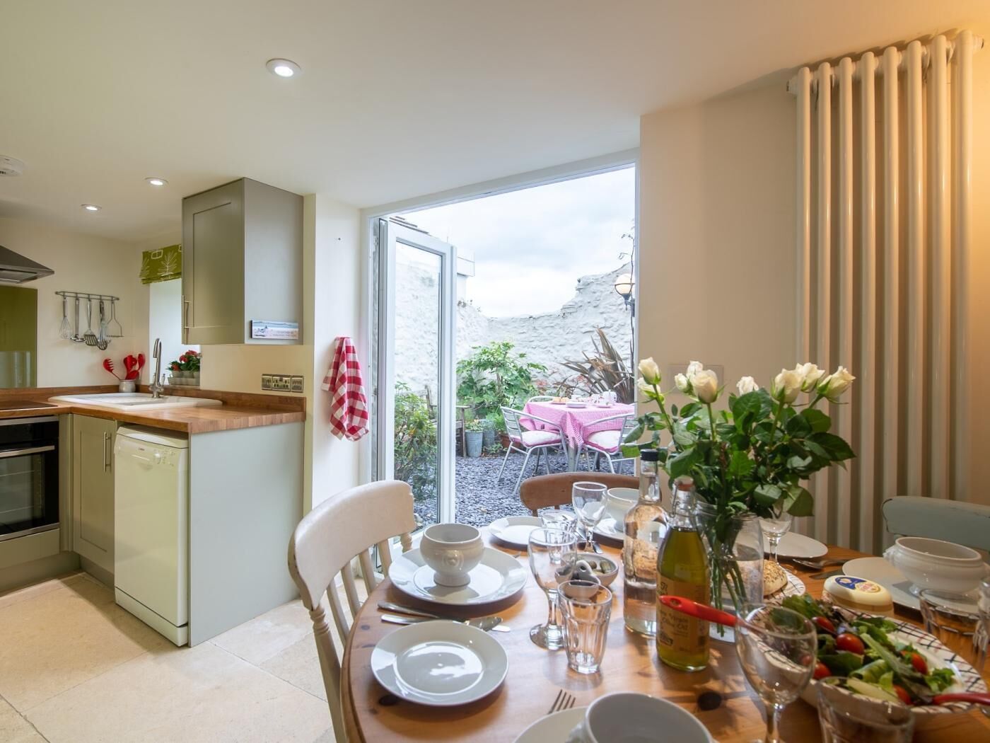 Comedor con mesa lista para dos, cocina equipada con lavavajillas y vistas al exterior.