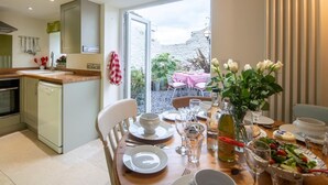 A dining area with a table set for two, a kitchen with a dishwasher, and a view of the outdoors. - 3 Bed in Bridport (oc-dc080) (Charmouth)