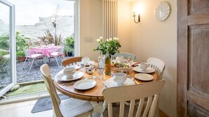 A dining area with a table set for four, a vase with flowers, and a clock on the wall. - 3 Bed in Bridport (oc-dc080) (Charmouth)