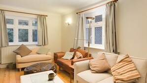 Ein Wohnzimmer mit einem gestreiften Sofa, einem braunen Ledersessel, einem beigen Sofa und einem Couchtisch mit zwei Tassen.