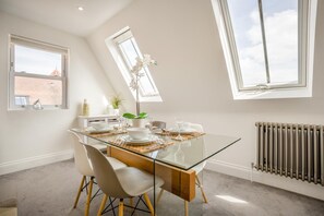 A dining area with a glass table, white chairs, and a view of the sky through a window. - 2 Bed in Swanage (oc-dc126) (Swanage)