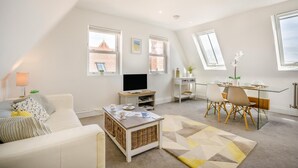 Ein stilvolles Wohnzimmer mit Sofa, Fernseher, Esstisch und einer kleinen Arbeitsnische.