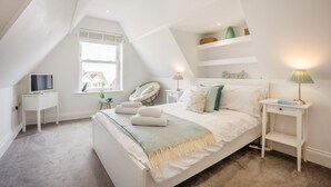 Ein Schlafzimmer mit Bett, Nachttischen, Fernseher, Fenster und schrägen Wänden.