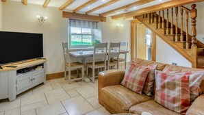 Un salon comprenant un téléviseur, un canapé, une table à manger avec des chaises et un escalier.