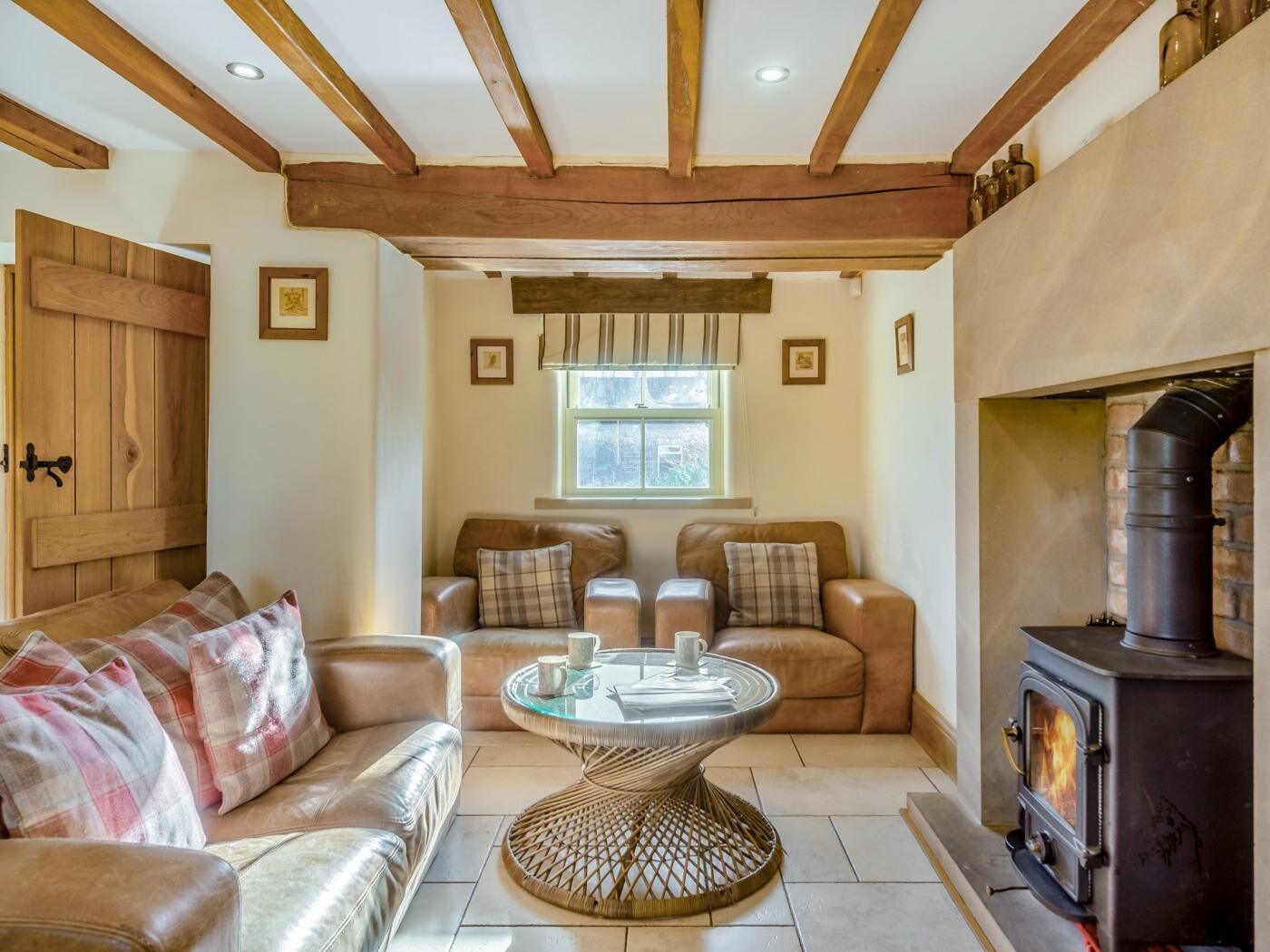 A cozy living room with a fireplace, leather sofas, a glass coffee table, and wooden beams on the ceiling.
