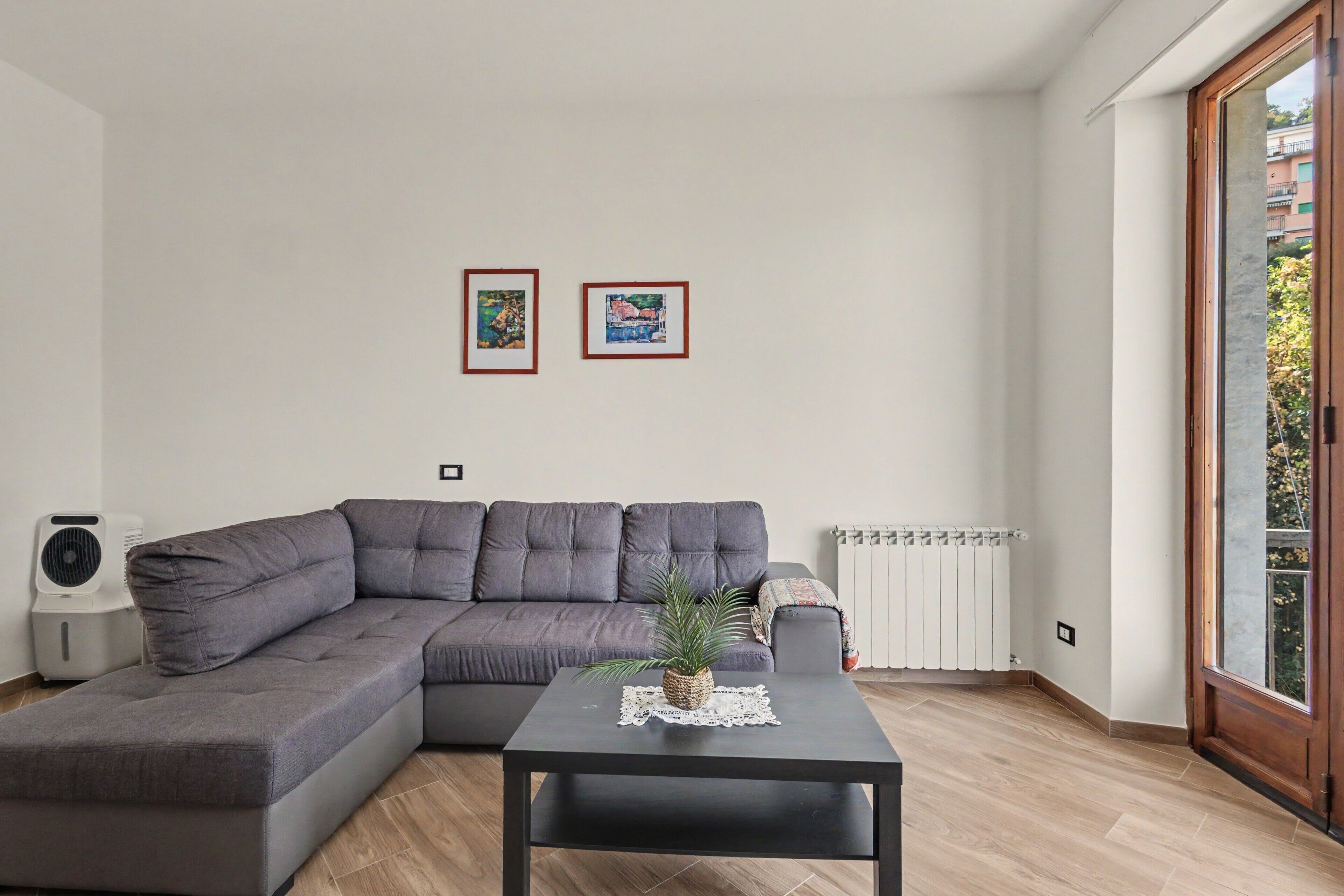 Un soggiorno moderno con un divano ad angolo grigio, un tavolino nero con una pianta e due opere d'arte appese al muro.
