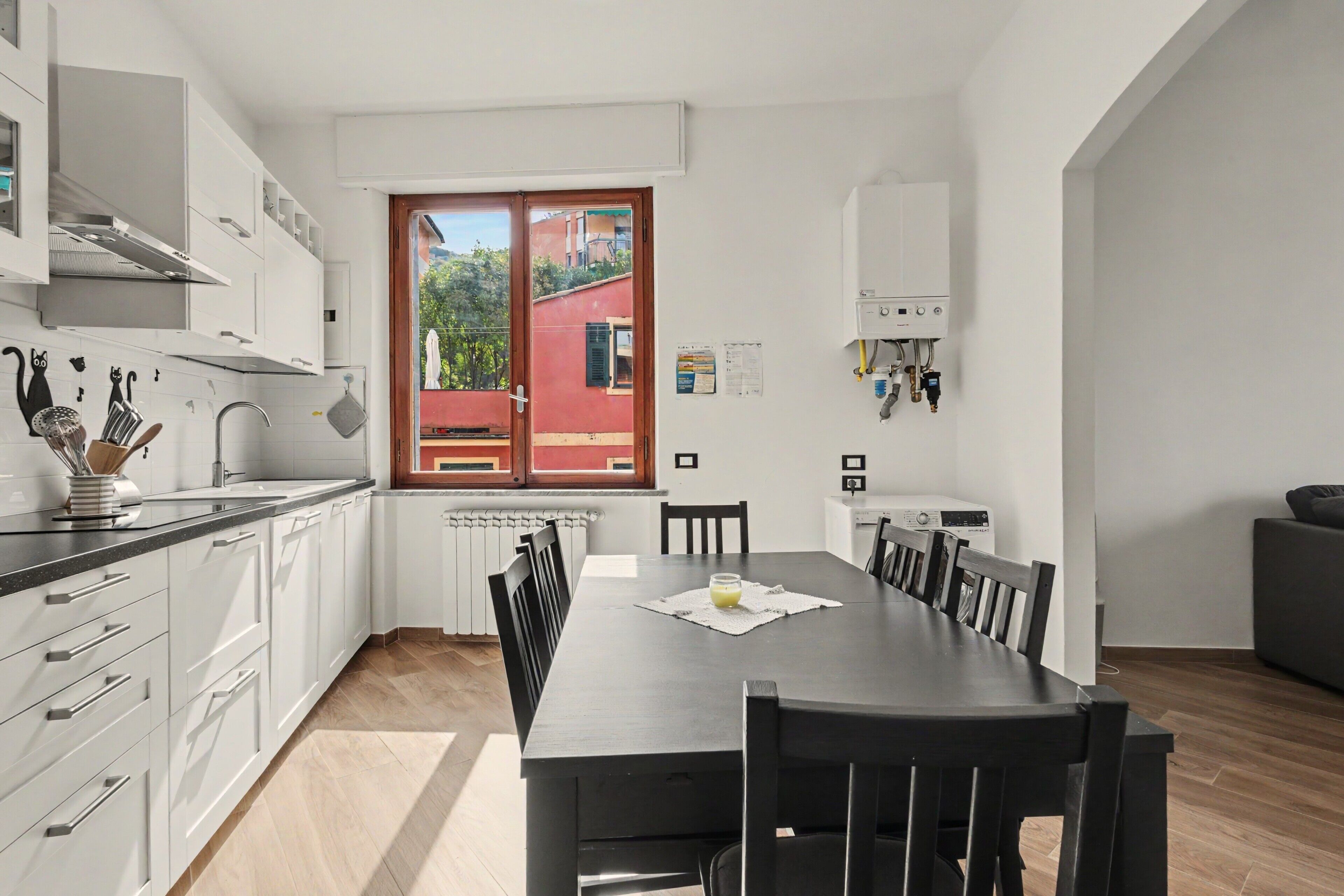 A modern kitchen with white cabinets, a dining table with chairs, and a view of a red building outside.