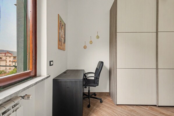 A room with a window, a desk, a chair, and a view of buildings outside.