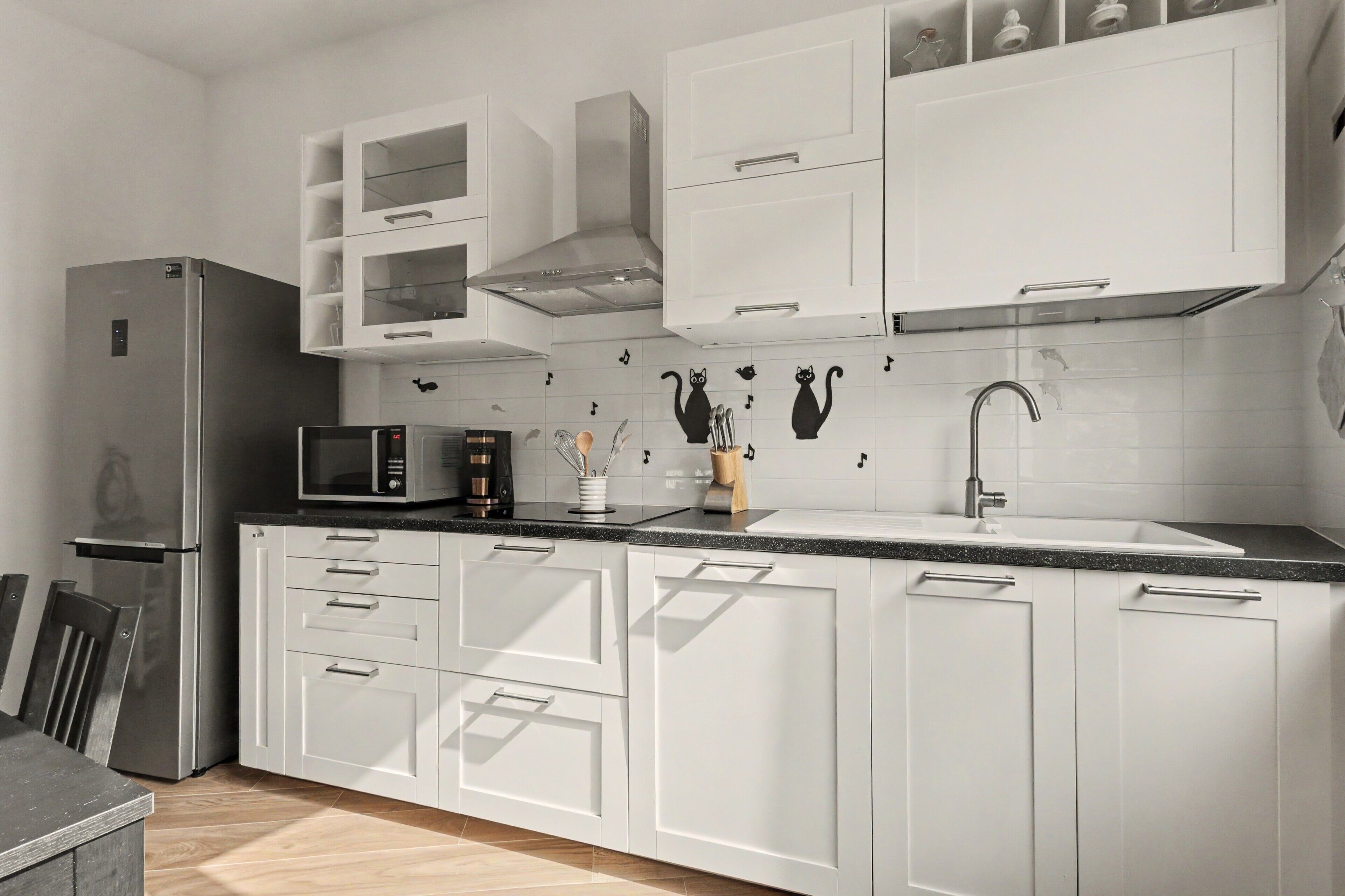 Una cucina moderna con mobili bianchi, un frigorifero in acciaio inossidabile, un forno a microonde e un lavello con rubinetto.