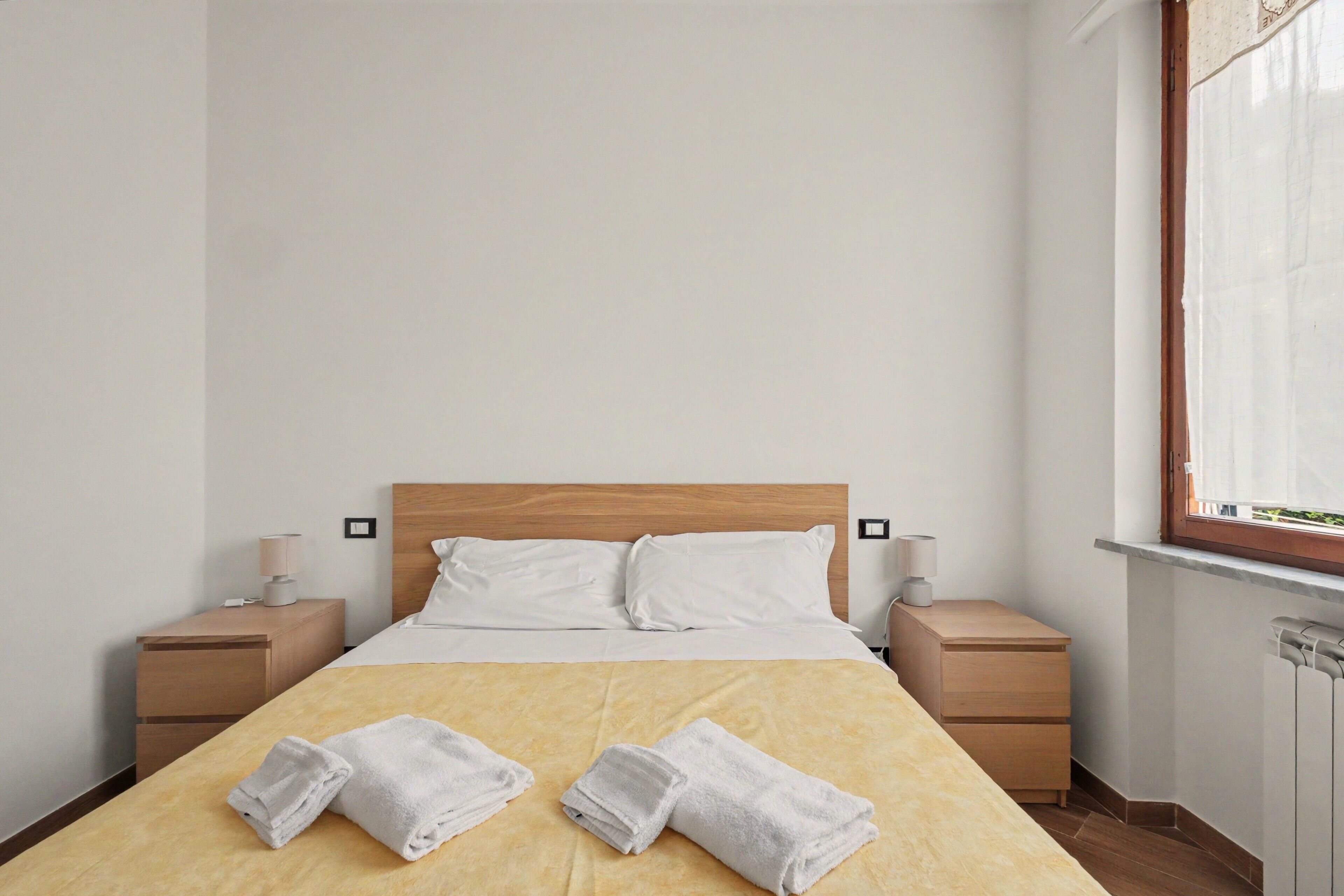 Una camera d'albergo con un letto, due comodini, una finestra e due asciugamani sul letto.