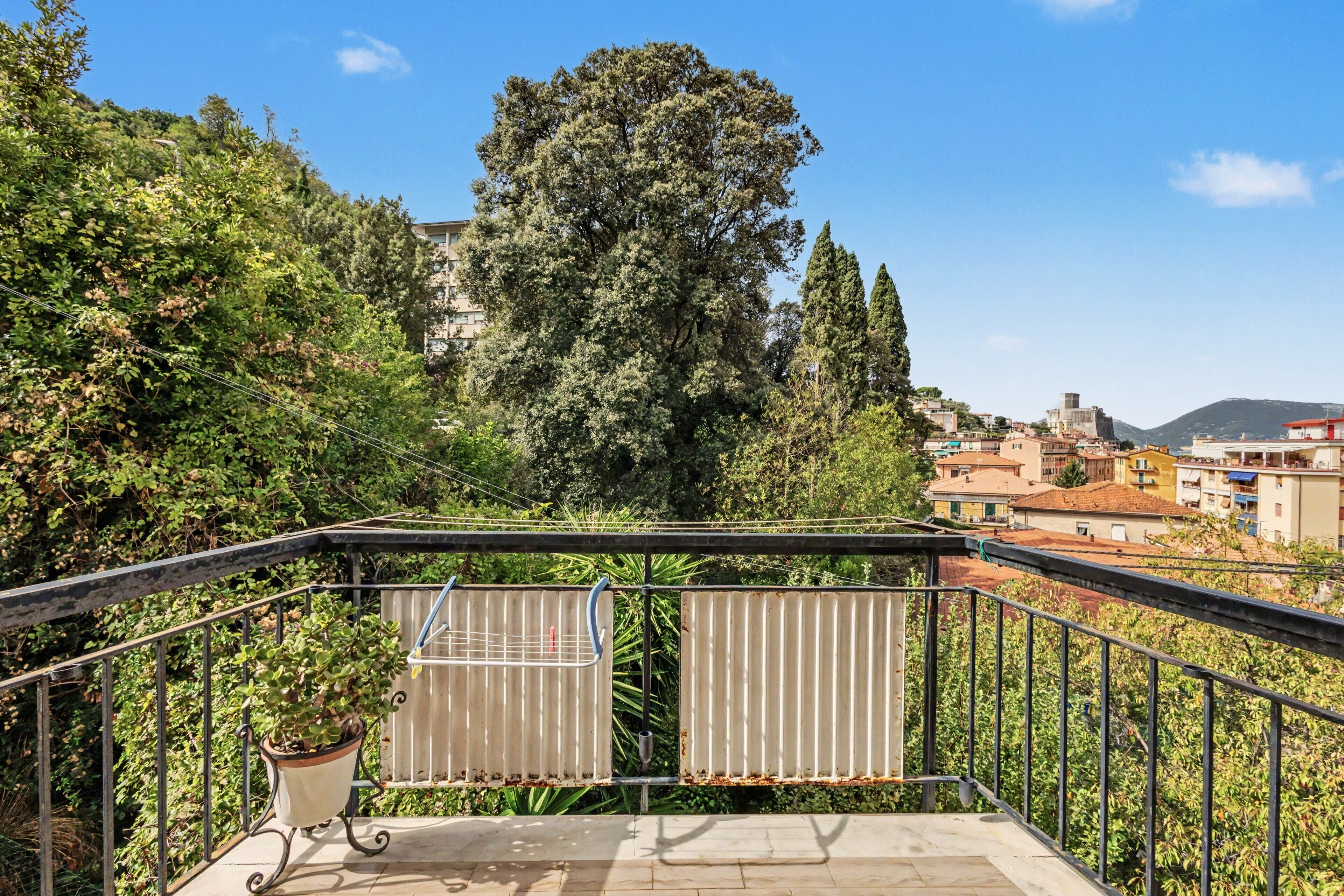 Un balcone con ringhiere in metallo, una pianta in vaso e vista su un paesaggio urbano con edifici e alberi.