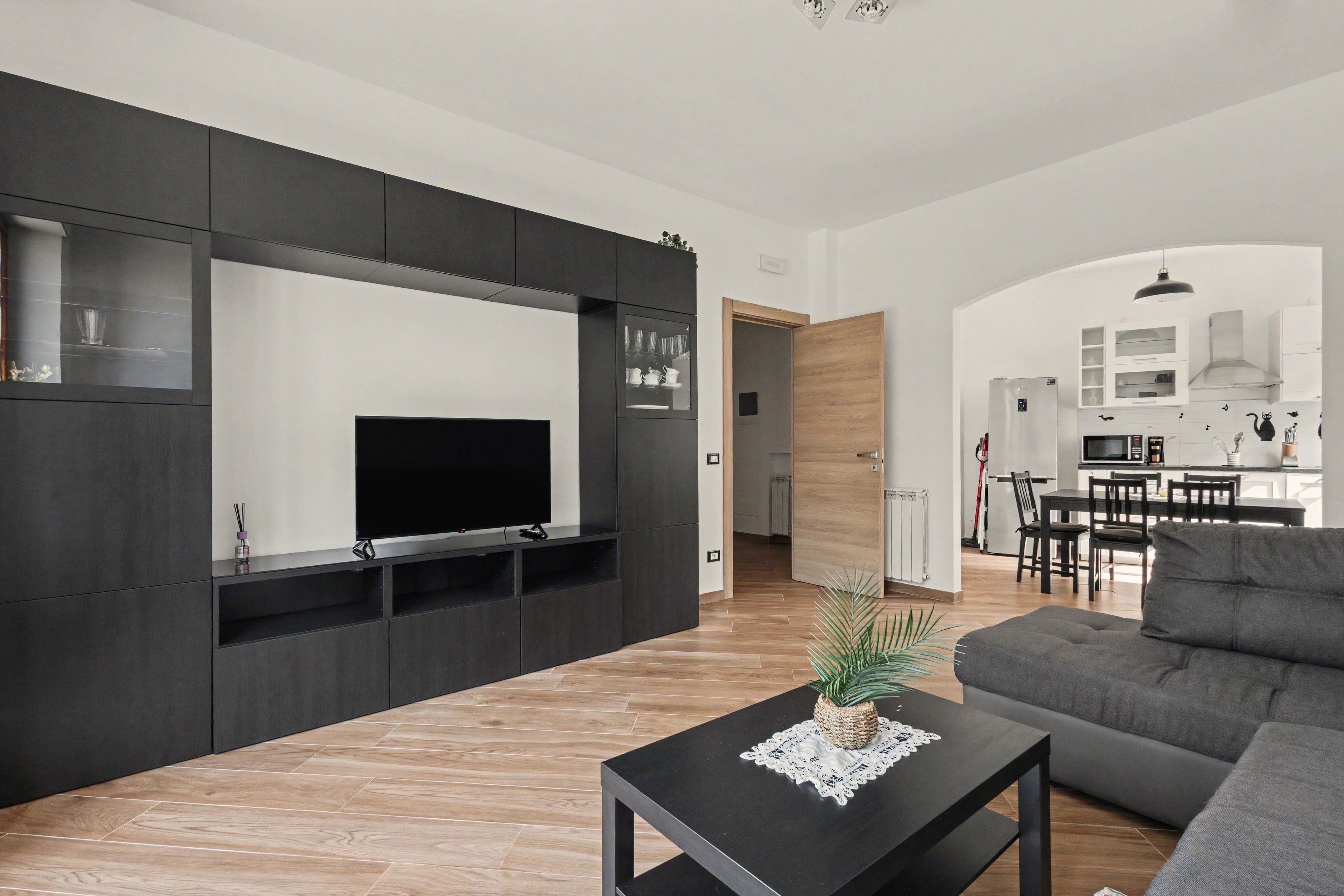 Un soggiorno moderno con una TV a schermo piatto, mobili scuri e un divano grigio.