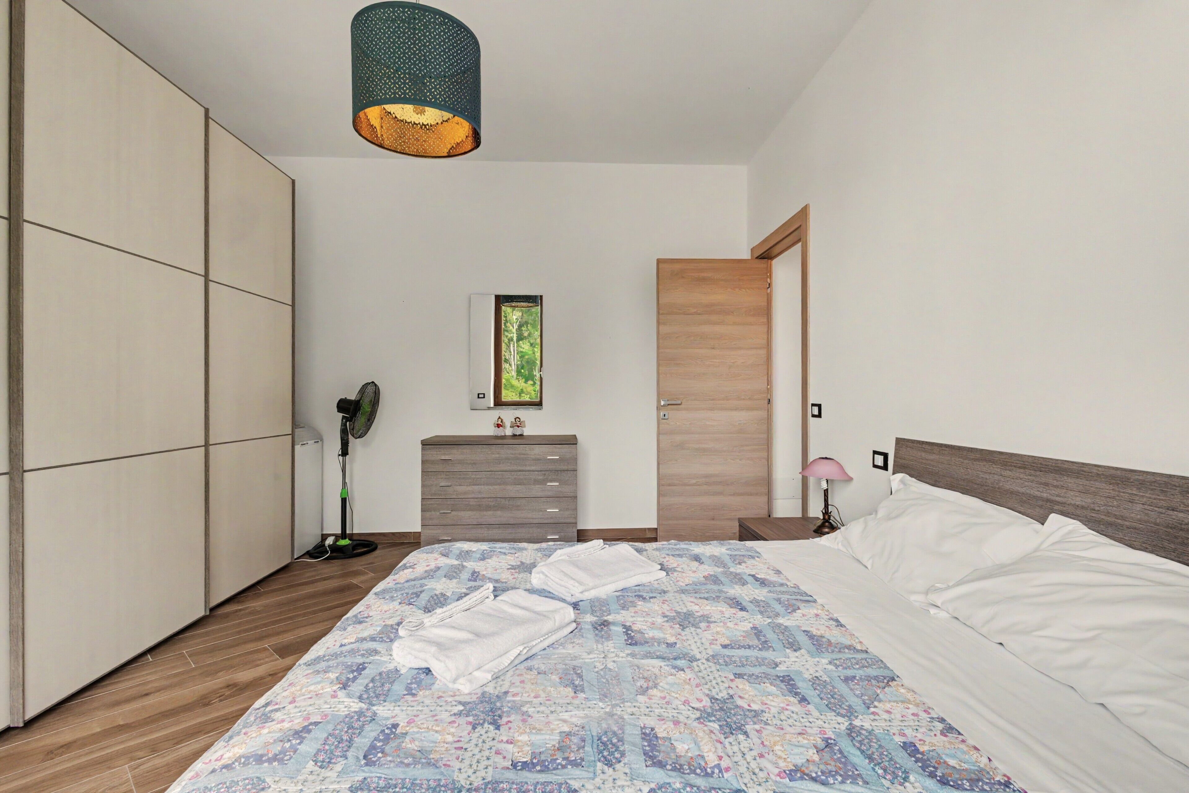 Une chambre à coucher avec un lit, une commode, une armoire, un ventilateur et une porte.