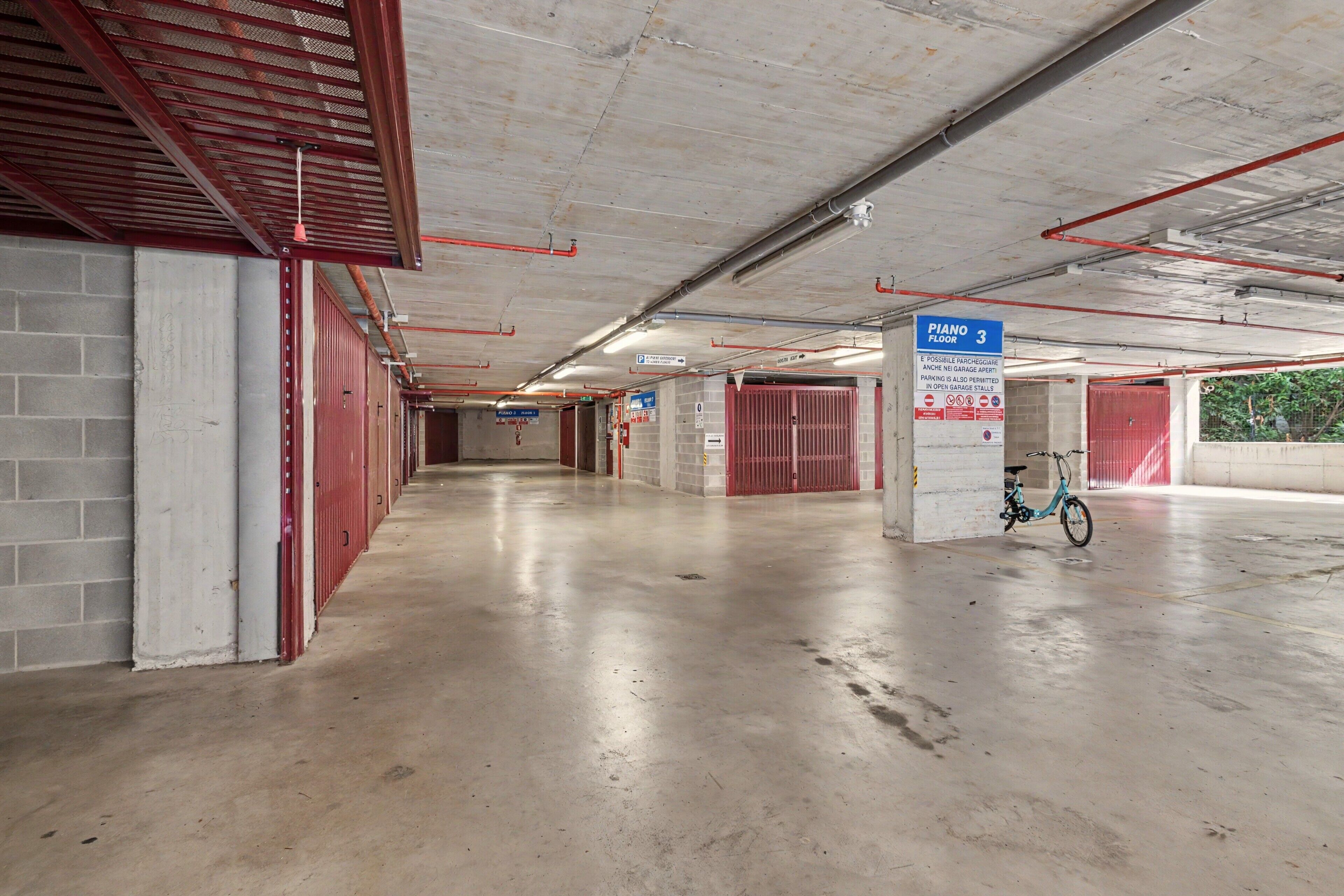 Un parcheggio multipiano con pavimenti in cemento, ringhiere in metallo rosso e un cartello blu che indica il terzo piano.