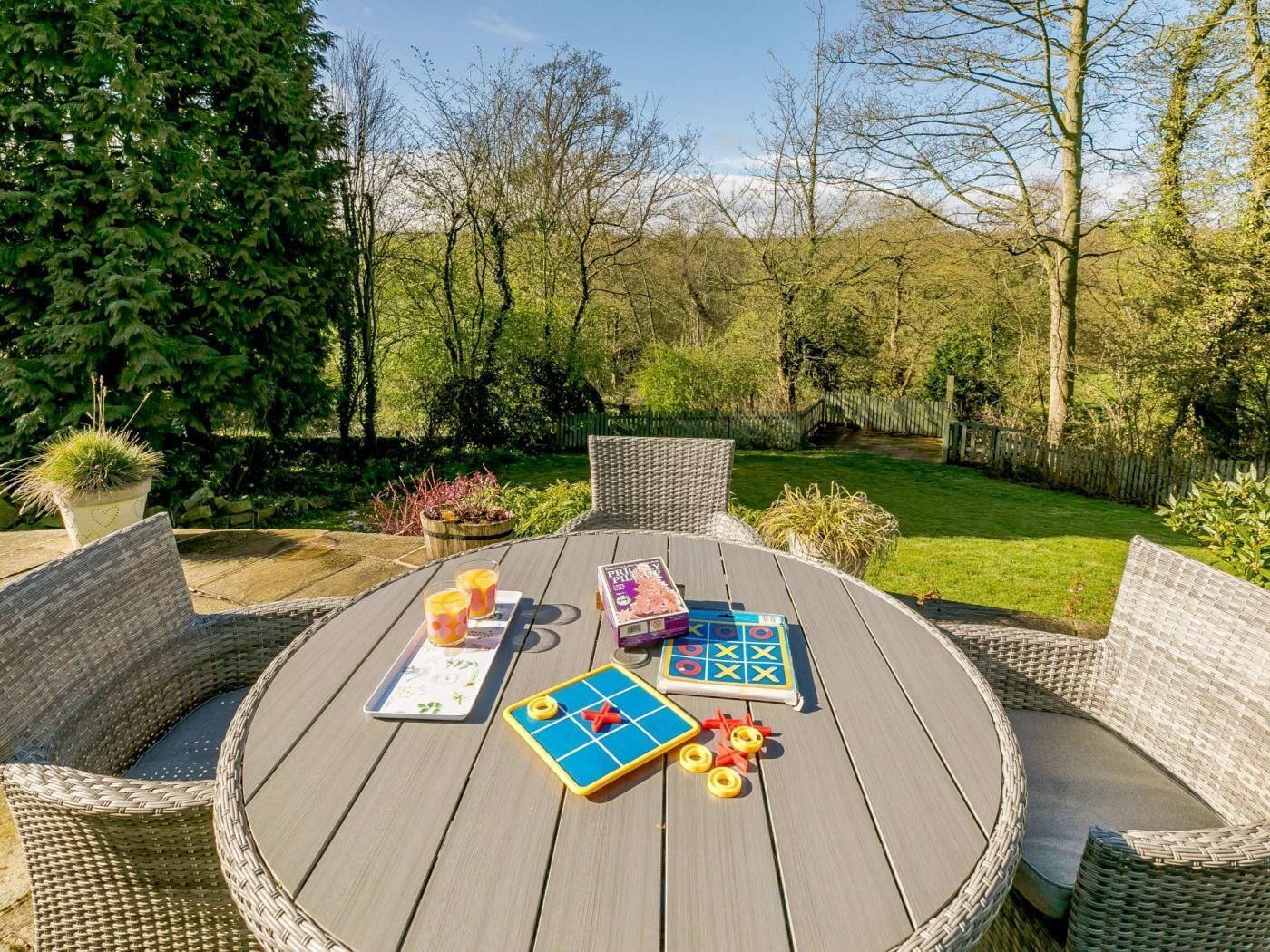 Une table ronde en bois, des chaises en osier, un jeu de société et un plateau avec des boissons.