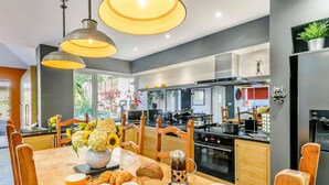 Una cocina moderna con comedor, que incluye una mesa de madera dispuesta con pan, cruasanes y un jarrón de flores.