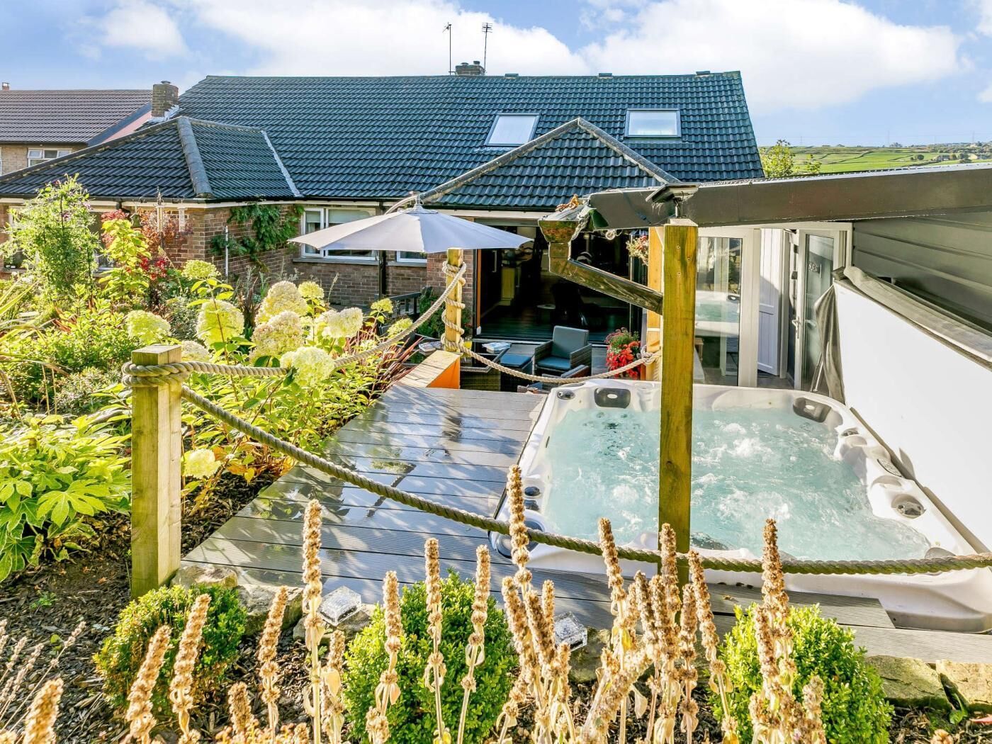 Un jardín en la azotea con jacuzzi, terraza de madera y abundante vegetación.