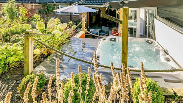 Un jardín en la azotea con jacuzzi, terraza de madera y abundante vegetación.