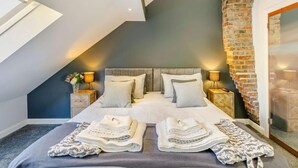 Un dormitorio con techo inclinado, pared de acento de ladrillo, una cama grande con múltiples almohadas, lámparas de noche y un tragaluz.