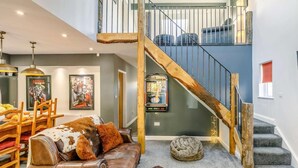 Un espacio habitable de varios niveles con una escalera, un sofá de cuero, un comedor y obras de arte en las paredes.