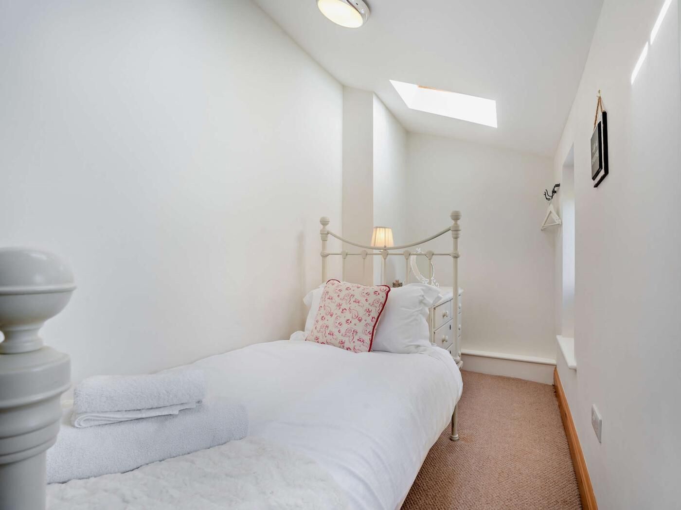 A bedroom with a white bed, a bedside lamp, a white radiator, and a skylight.