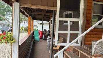A covered porch with a bench, a table, a fan, and a window.