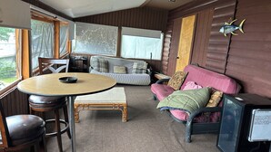 A cozy room with a round table, a sofa, a television, and a window.