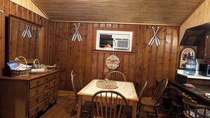 A wooden-paneled room with a dining table, chairs, a kitchen area with a microwave, and a window.
