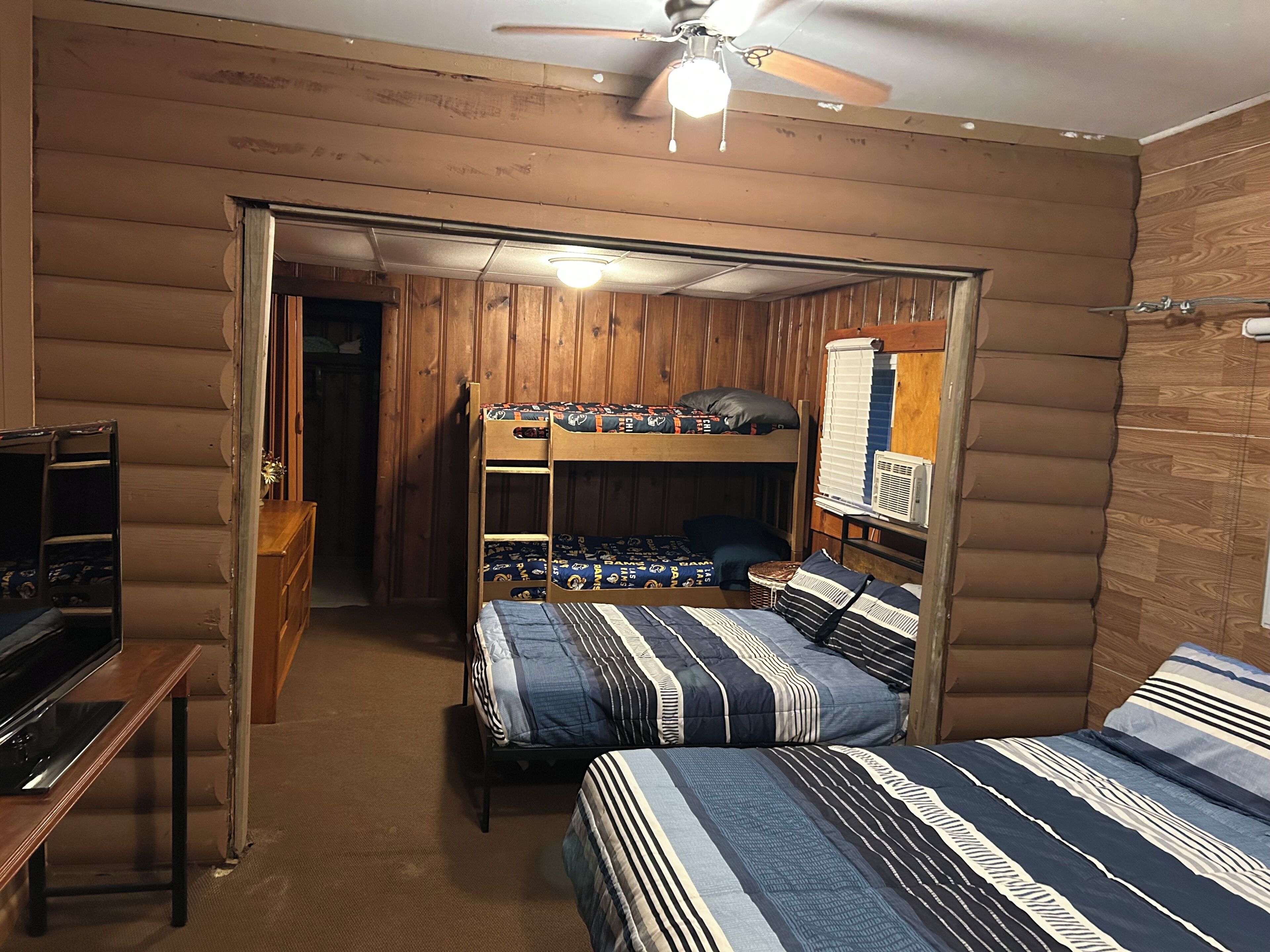 Een kamer met stapelbedden, een plafondventilator, een bureau en een raam met jaloezieën.