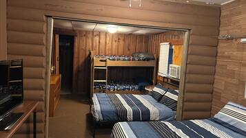 Een kamer met stapelbedden, een plafondventilator, een bureau en een raam met jaloezieën.