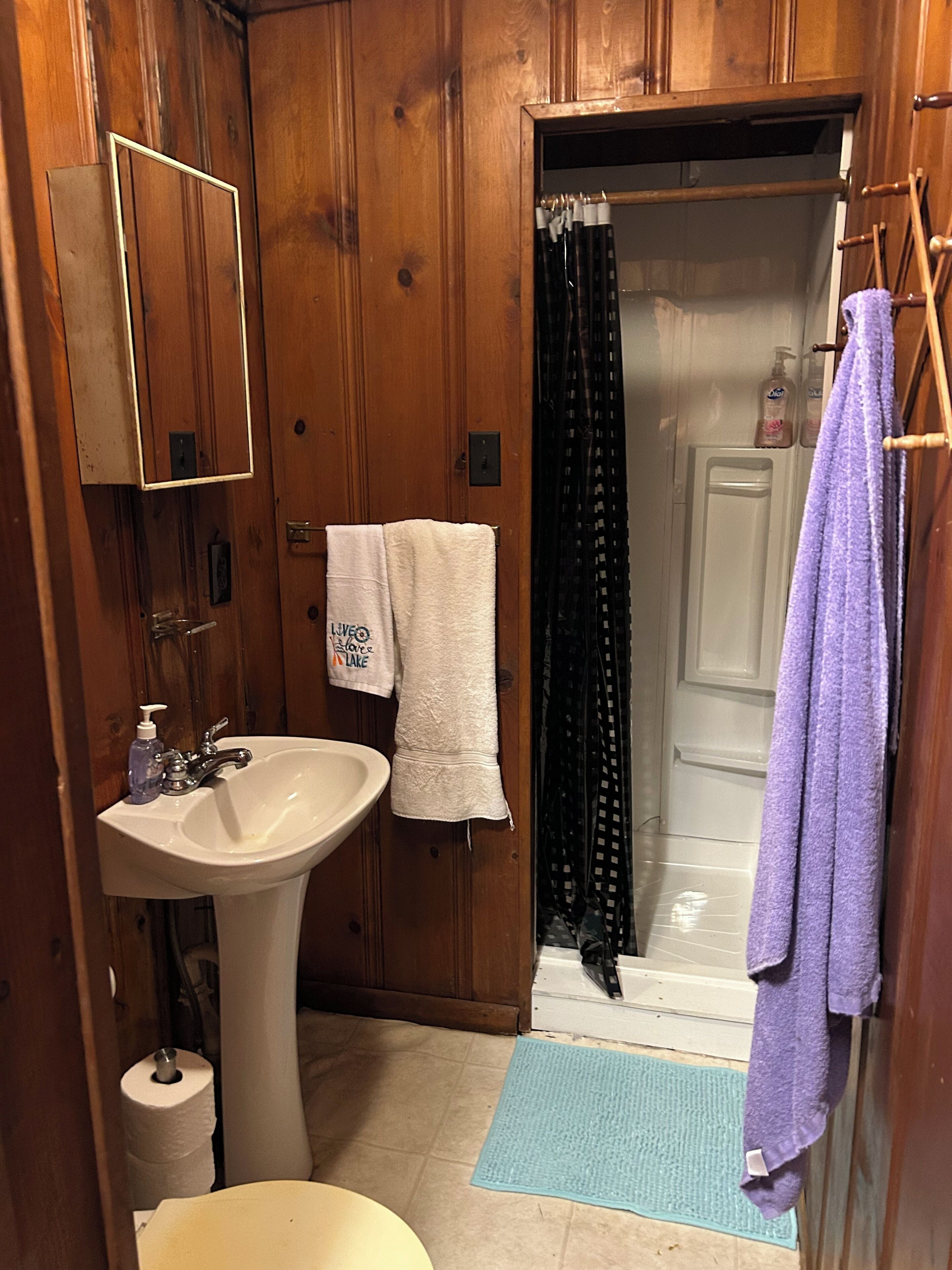 Une salle de bain en bois avec un lavabo blanc, un miroir, un porte-serviettes et un rideau de douche.