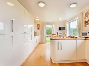A modern kitchen with white cabinetry, a wooden countertop, and a large window providing a view of greenery. - 4 Bed in Swanage (oc-75639) (Studland)