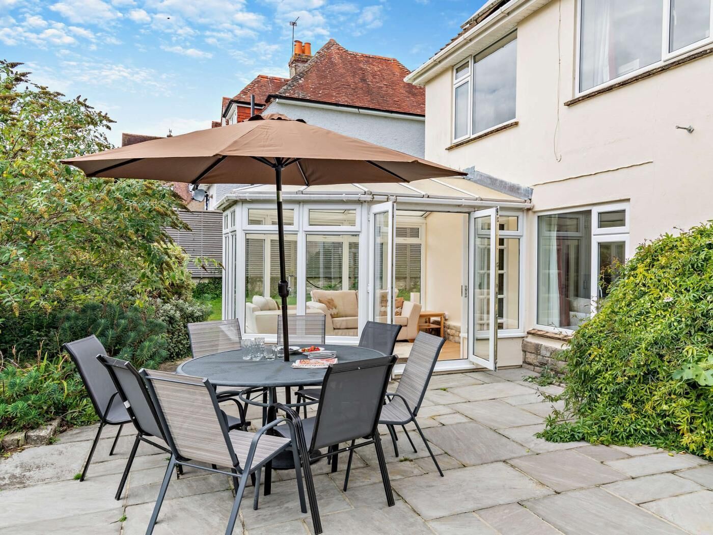A patio with a round table and chairs, a large umbrella, and a conservatory with furniture.