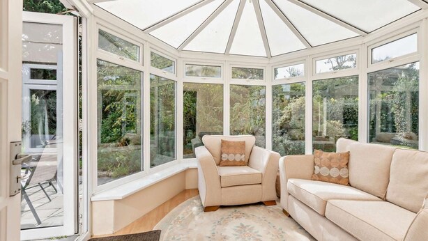 Ein Wintergarten mit Glasdecke, beigen Sofas und einem gemusterten Teppich.