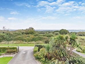 A paved pathway leading through a lush garden with various plants and a view of the sea in the distance. - 4 Bed in Swanage (oc-75639) (Studland)