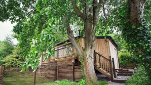 A wooden cabin with a wooden staircase leading up to a deck, surrounded by greenery. - 1 Bed in Abergavenny (oc-75206) (Gilwern)