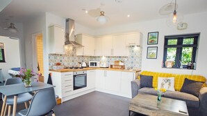 A modern kitchen with white cabinets, a central island, and a dining area with a gray table and chairs. - 1 Bed in Abergavenny (oc-75206) (Gilwern)