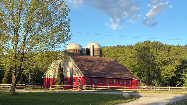 A red barn with two silos, surrounded by a wooden fence, and a gravel path leading to it.