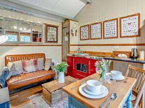 Une cuisine chaleureuse avec un poêle rouge, des meubles en bois et une table à manger dressée pour deux personnes.